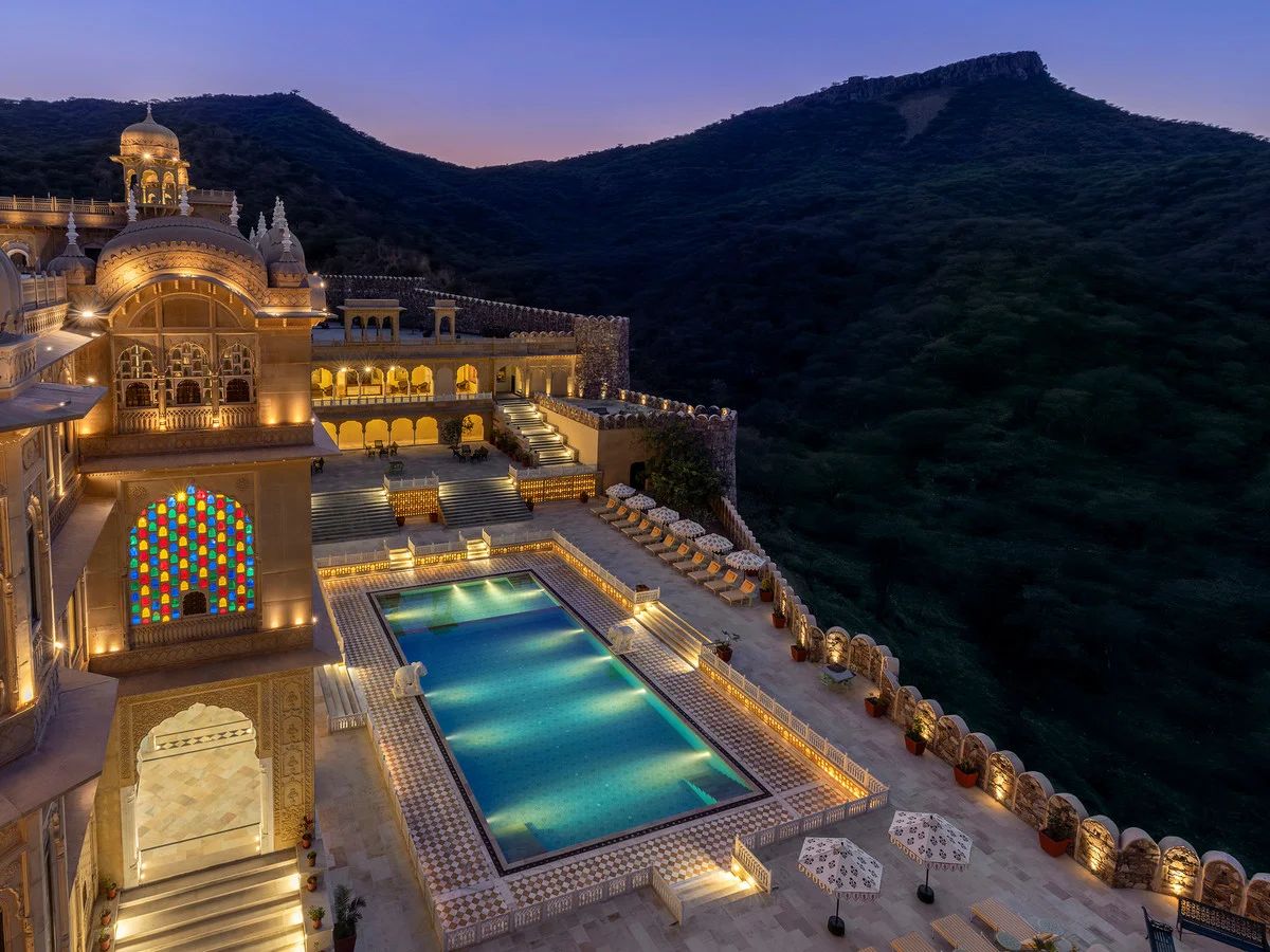 Illuminated palace arches and a turquoise pool beneath the hills at twilight